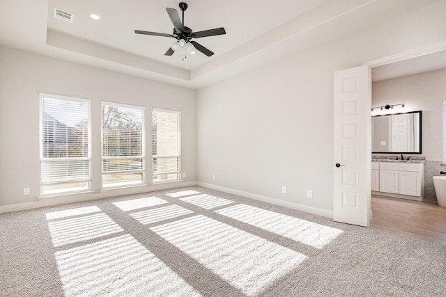 unfurnished bedroom featuring connected bathroom, ceiling fan, sink, a tray ceiling, and light carpet