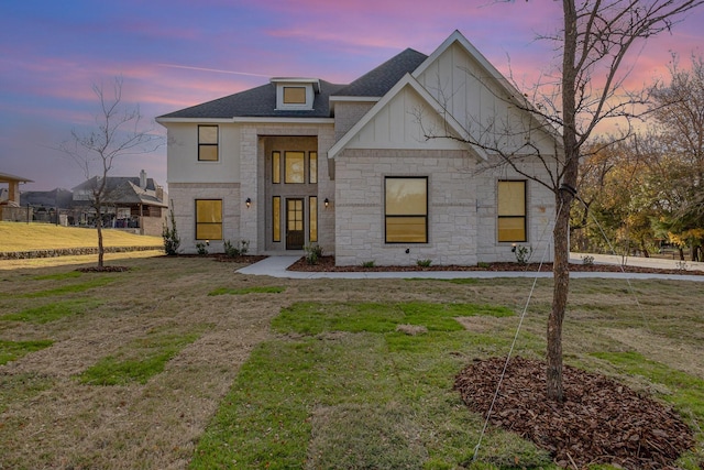 view of front of house with stone siding, a shingled roof, a lawn, and board and batten siding