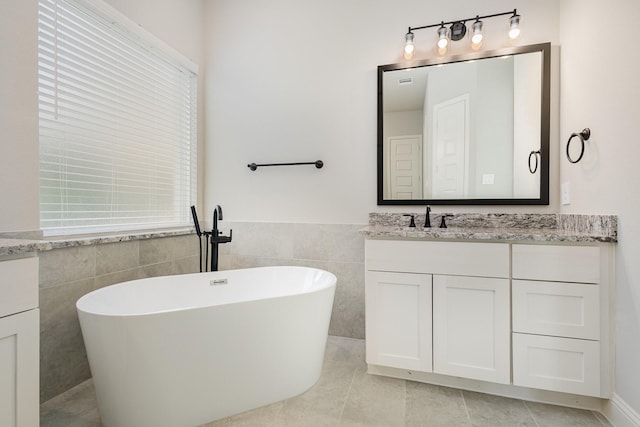 bathroom with tile patterned flooring, vanity, a tub, and tile walls