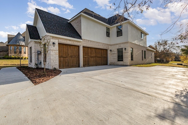 view of home's exterior with stucco siding, a shingled roof, an attached garage, stone siding, and driveway