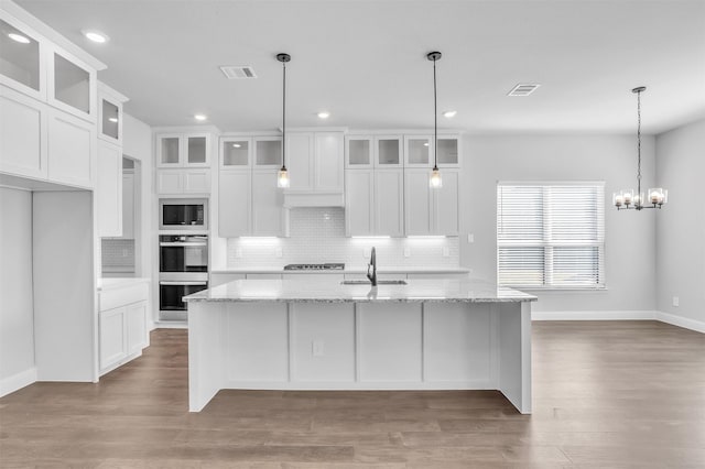 kitchen with light stone countertops, appliances with stainless steel finishes, white cabinetry, and a kitchen island with sink