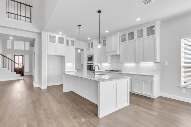 kitchen featuring a center island with sink, light stone counters, white cabinetry, and sink