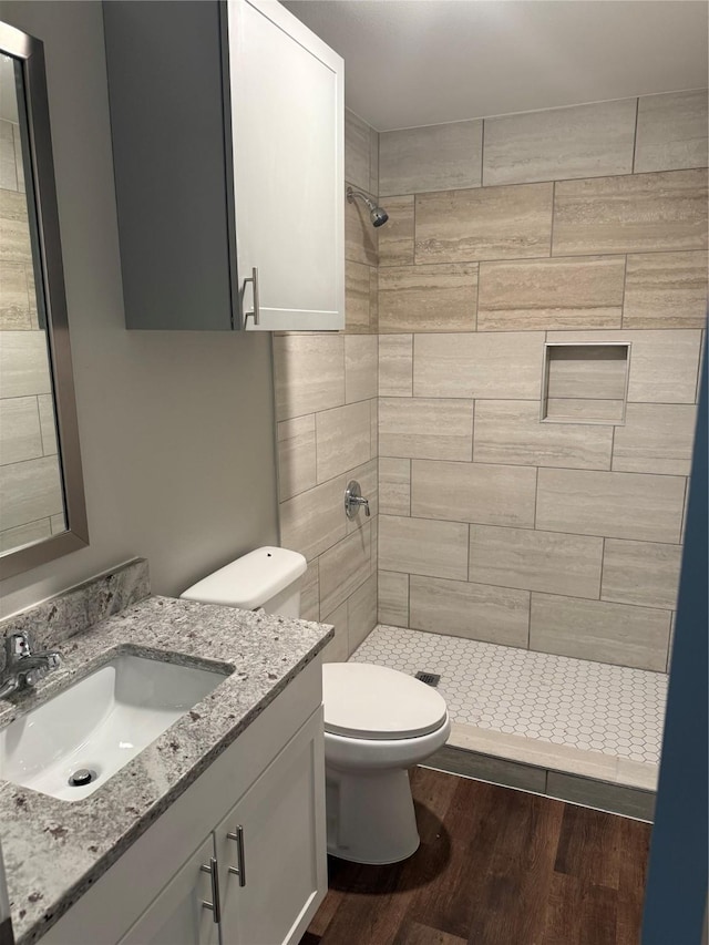 bathroom featuring wood-type flooring, toilet, vanity, and a tile shower