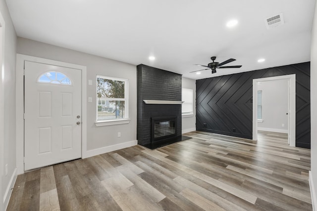 entrance foyer featuring ceiling fan, light wood-type flooring, wood walls, and a brick fireplace