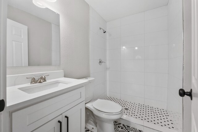 bathroom with a tile shower, vanity, and toilet