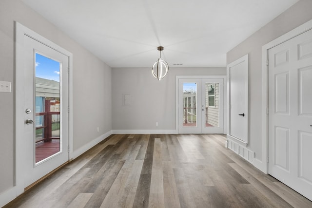 unfurnished dining area featuring french doors, light hardwood / wood-style floors, and an inviting chandelier