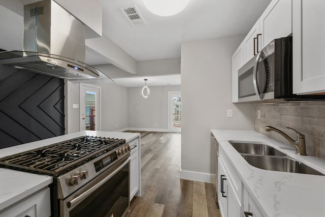 kitchen featuring dark wood-type flooring, white cabinets, wall chimney range hood, appliances with stainless steel finishes, and light stone counters