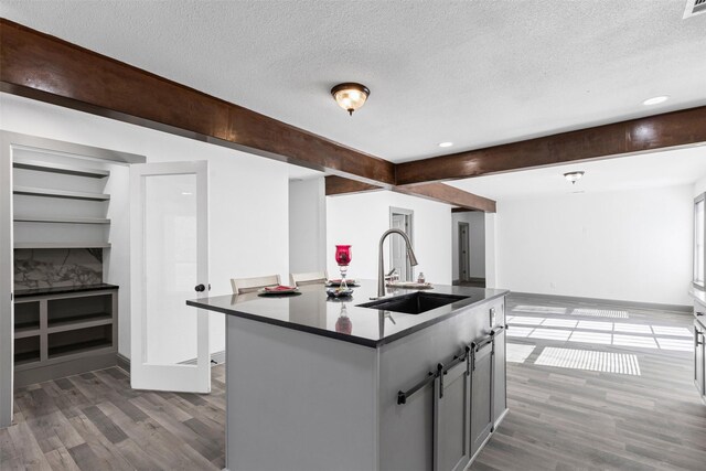 kitchen with a textured ceiling, a kitchen island with sink, sink, beam ceiling, and gray cabinets