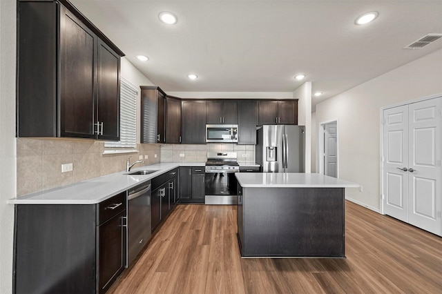 kitchen with dark brown cabinetry, sink, stainless steel appliances, a kitchen island, and hardwood / wood-style flooring