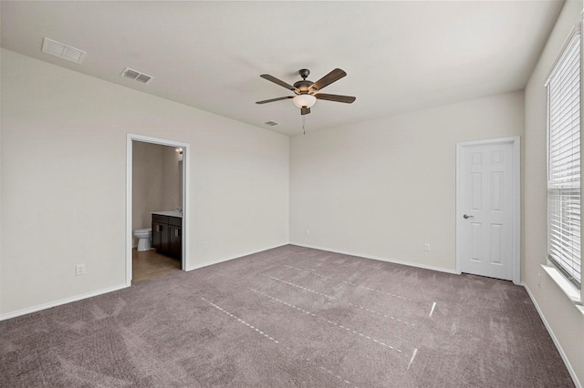 unfurnished bedroom featuring carpet flooring, multiple windows, ensuite bathroom, and ceiling fan