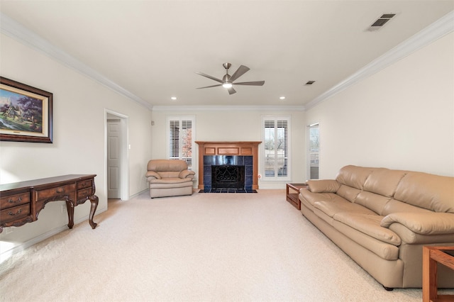 living room with a tile fireplace, light colored carpet, a ceiling fan, visible vents, and ornamental molding