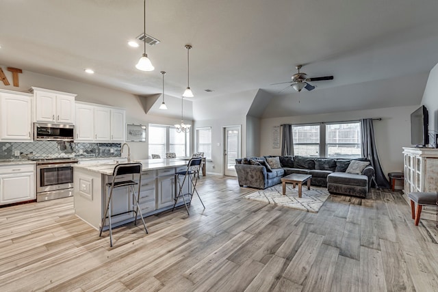 kitchen with a breakfast bar area, decorative light fixtures, appliances with stainless steel finishes, a kitchen island with sink, and white cabinets