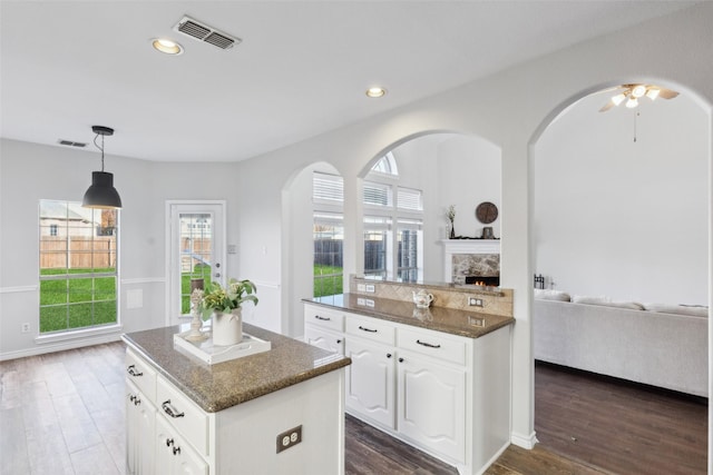 kitchen with a center island, a stone fireplace, dark stone countertops, dark hardwood / wood-style flooring, and white cabinetry