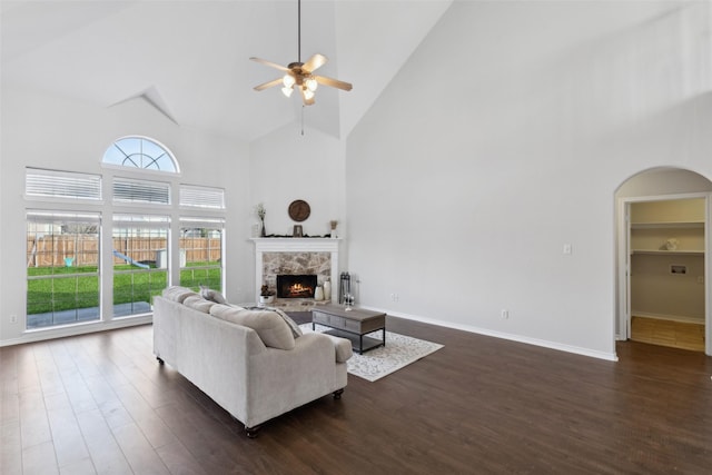 living room with ceiling fan, a stone fireplace, dark hardwood / wood-style floors, and high vaulted ceiling