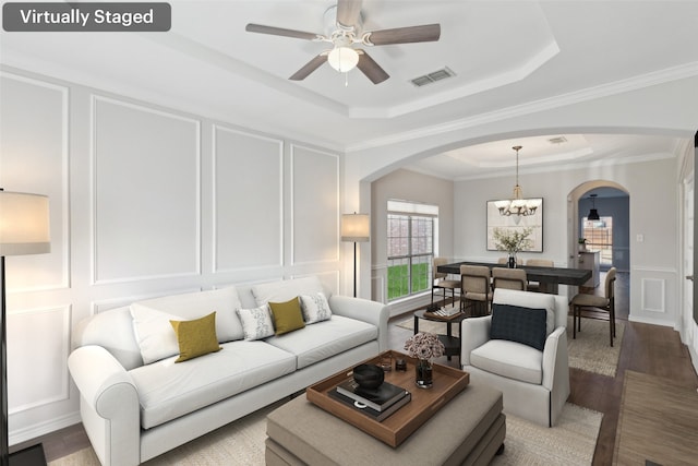 living room with a tray ceiling, crown molding, wood-type flooring, and ceiling fan with notable chandelier