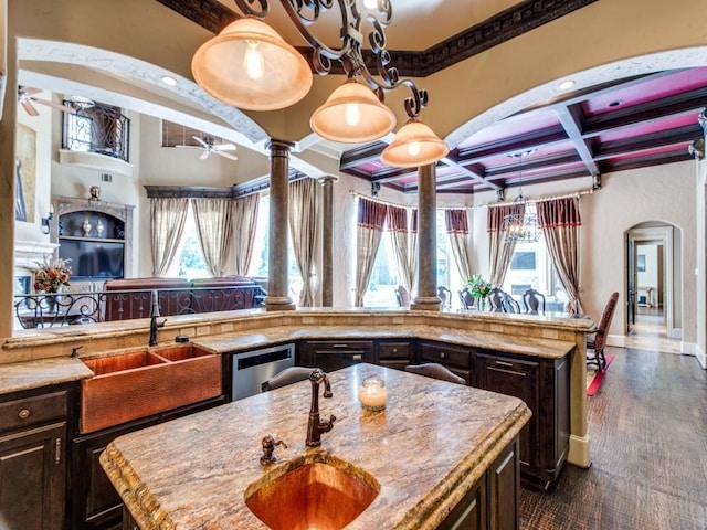 kitchen with sink, coffered ceiling, decorative columns, dark brown cabinets, and a center island with sink