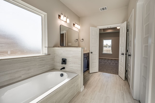 bathroom featuring tile patterned floors, vanity, and a relaxing tiled tub