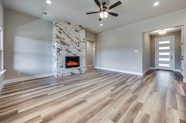 unfurnished living room with ceiling fan, a large fireplace, and light hardwood / wood-style floors