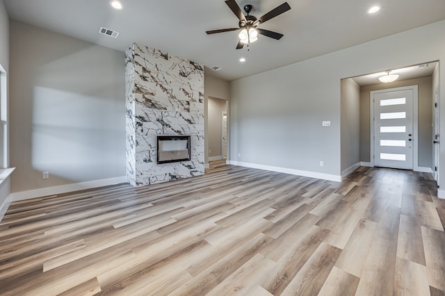 unfurnished living room featuring ceiling fan, a large fireplace, and light hardwood / wood-style flooring