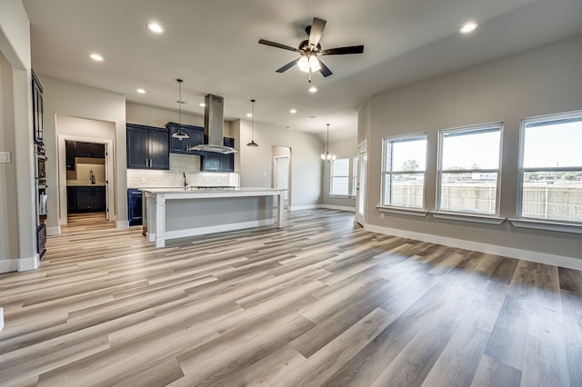 unfurnished living room featuring ceiling fan with notable chandelier and light hardwood / wood-style floors