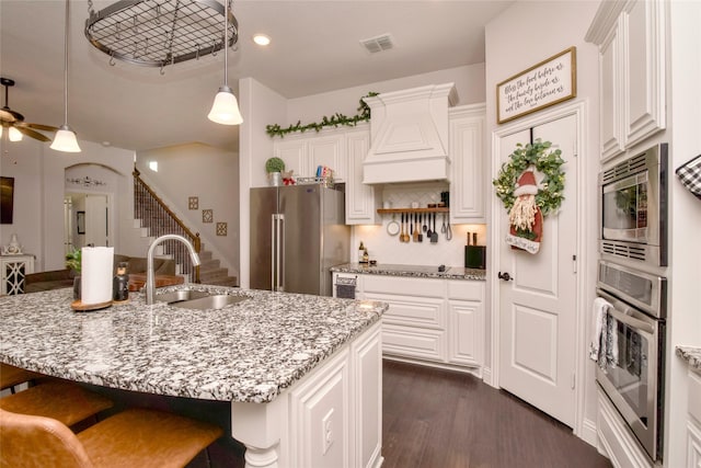 kitchen with appliances with stainless steel finishes, dark hardwood / wood-style flooring, light stone counters, a kitchen island with sink, and sink