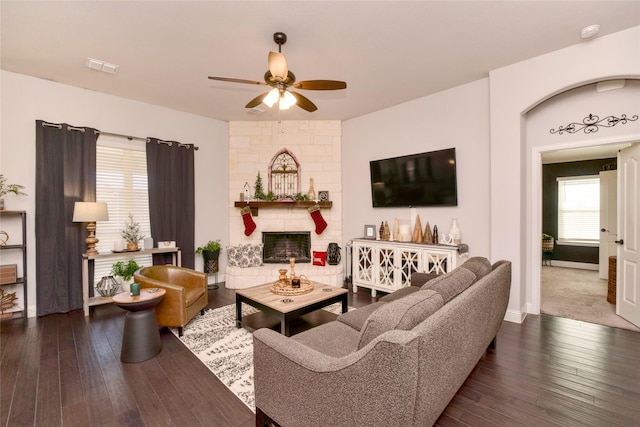 living room featuring a stone fireplace, ceiling fan, and dark hardwood / wood-style floors