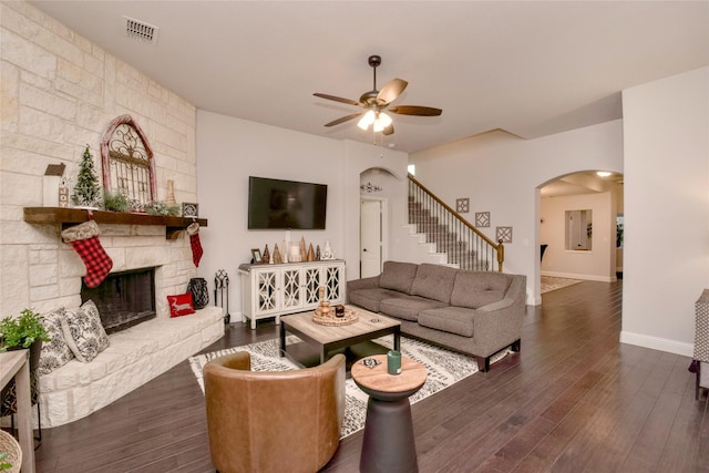 living room featuring a stone fireplace, dark wood-type flooring, and ceiling fan