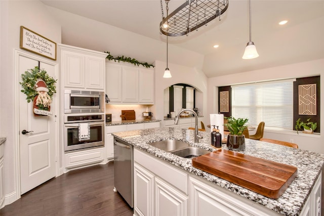 kitchen featuring appliances with stainless steel finishes, decorative light fixtures, sink, white cabinets, and a center island with sink