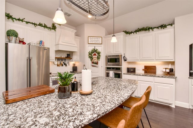 kitchen with hanging light fixtures, white cabinets, stainless steel appliances, light stone countertops, and backsplash