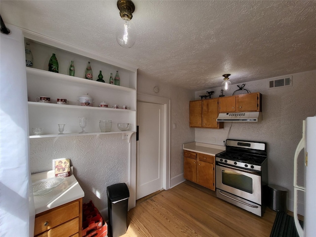 kitchen with a textured ceiling, stainless steel gas range oven, light hardwood / wood-style floors, and fridge