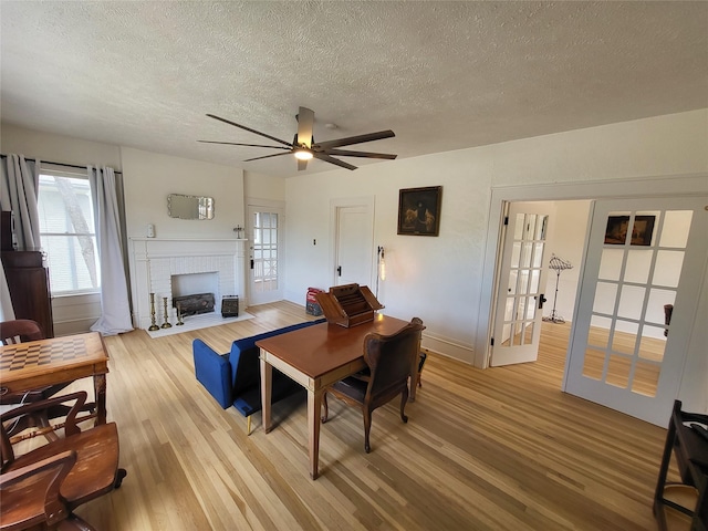 living room with french doors, light hardwood / wood-style flooring, ceiling fan, a fireplace, and a textured ceiling