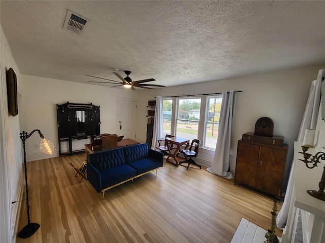 living room featuring a textured ceiling, light wood-type flooring, and ceiling fan