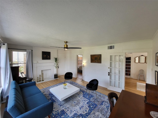 living room with ceiling fan, wood-type flooring, a textured ceiling, and a brick fireplace