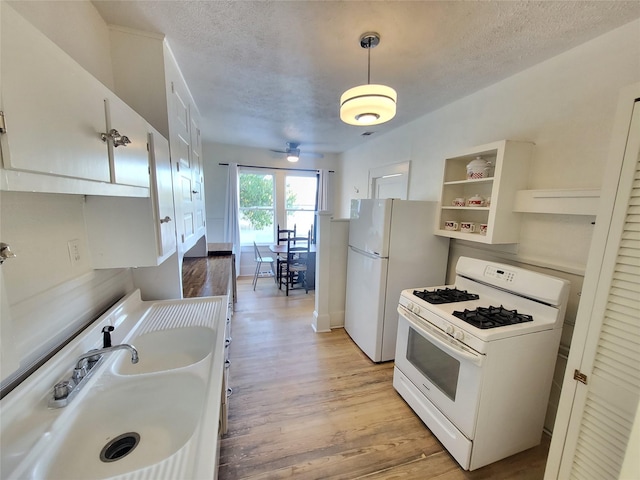 kitchen featuring light wood-type flooring, white appliances, sink, white cabinetry, and hanging light fixtures