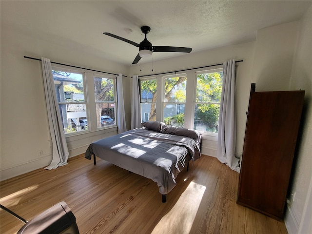 bedroom featuring multiple windows, a textured ceiling, light hardwood / wood-style floors, and ceiling fan