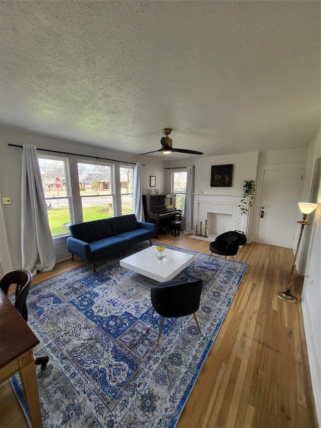 living room with a fireplace, ceiling fan, a textured ceiling, and light hardwood / wood-style flooring