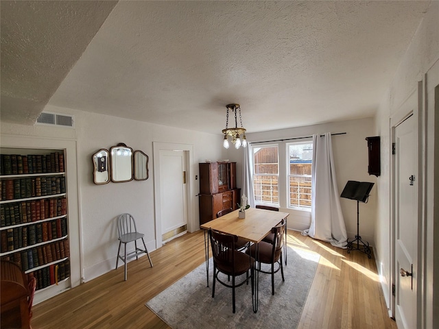 dining space featuring a chandelier, a textured ceiling, and light wood-type flooring