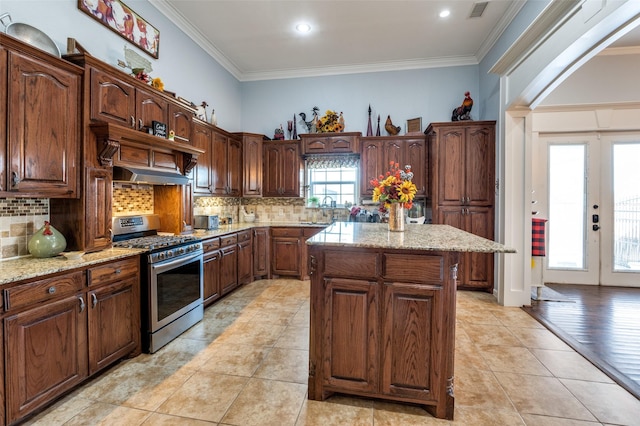 kitchen with french doors, crown molding, backsplash, a kitchen island, and gas range