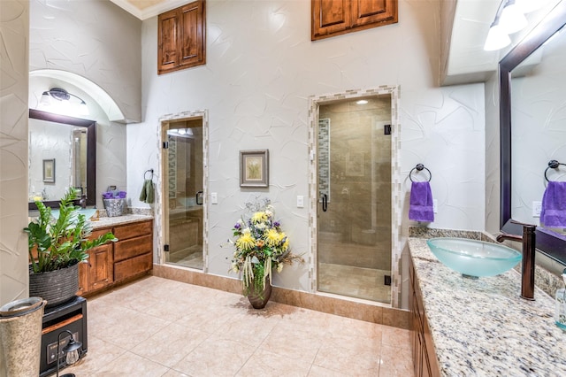 bathroom featuring a stall shower, tile patterned flooring, two vanities, and a sink