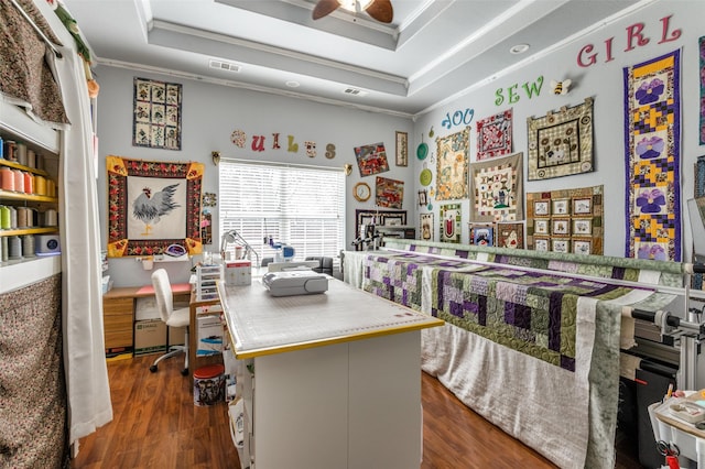 office space with visible vents, a ceiling fan, wood finished floors, a tray ceiling, and crown molding