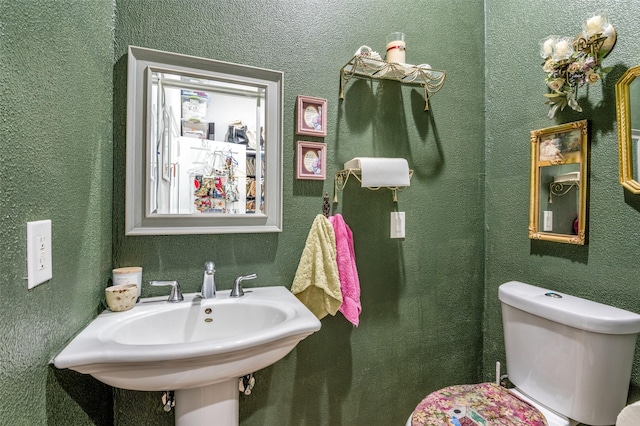 half bath with toilet, a textured wall, and a sink