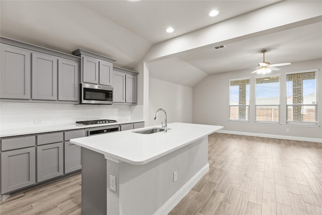 kitchen featuring gray cabinetry, lofted ceiling, a center island with sink, sink, and stainless steel appliances