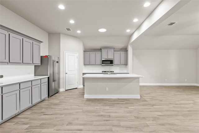 kitchen with appliances with stainless steel finishes, gray cabinetry, a kitchen island with sink, light hardwood / wood-style flooring, and lofted ceiling