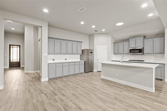 kitchen with light wood-type flooring, gray cabinetry, stainless steel appliances, a kitchen island with sink, and lofted ceiling