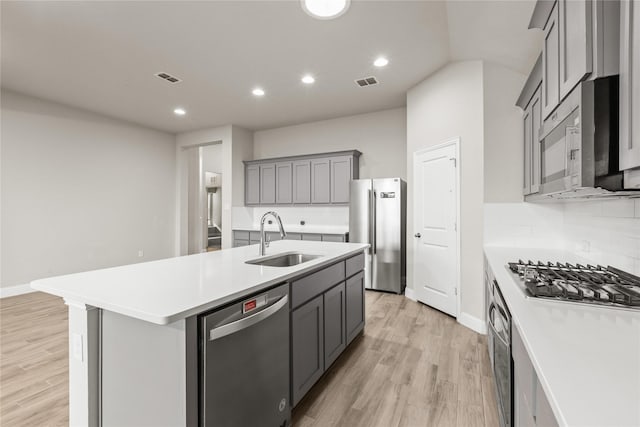 kitchen with a center island with sink, sink, gray cabinets, light hardwood / wood-style floors, and stainless steel appliances