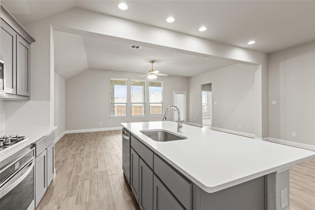 kitchen with a kitchen island with sink, sink, appliances with stainless steel finishes, and light hardwood / wood-style flooring