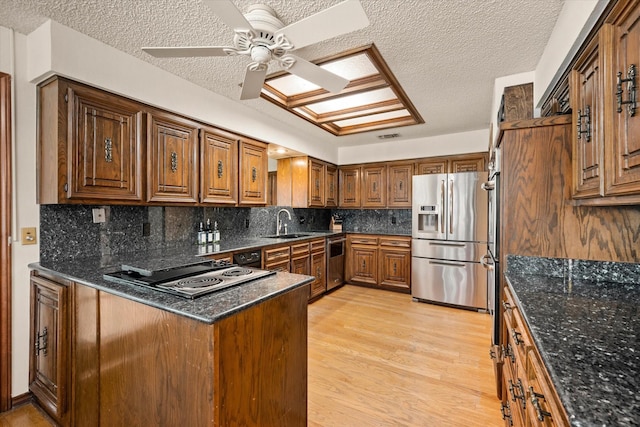 kitchen with stainless steel appliances, light hardwood / wood-style flooring, dark stone counters, a textured ceiling, and decorative backsplash