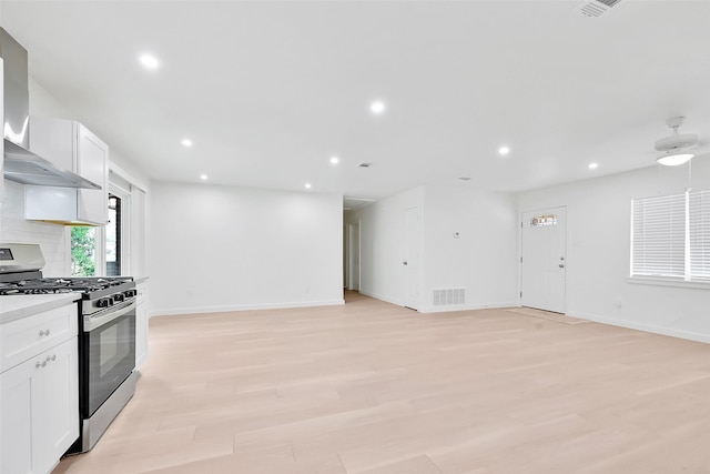 kitchen with backsplash, gas range, wall chimney range hood, white cabinets, and light hardwood / wood-style floors