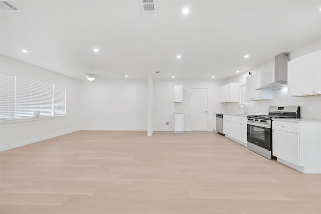 kitchen with white cabinets, wall chimney range hood, sink, light hardwood / wood-style floors, and stainless steel appliances