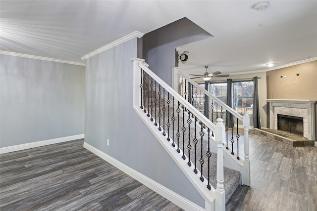 stairs featuring a stone fireplace, ceiling fan, wood-type flooring, and ornamental molding